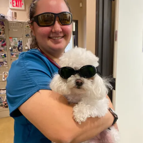 Woman in blue scrubs holding white fluffy dog while they both wear sunglasses.